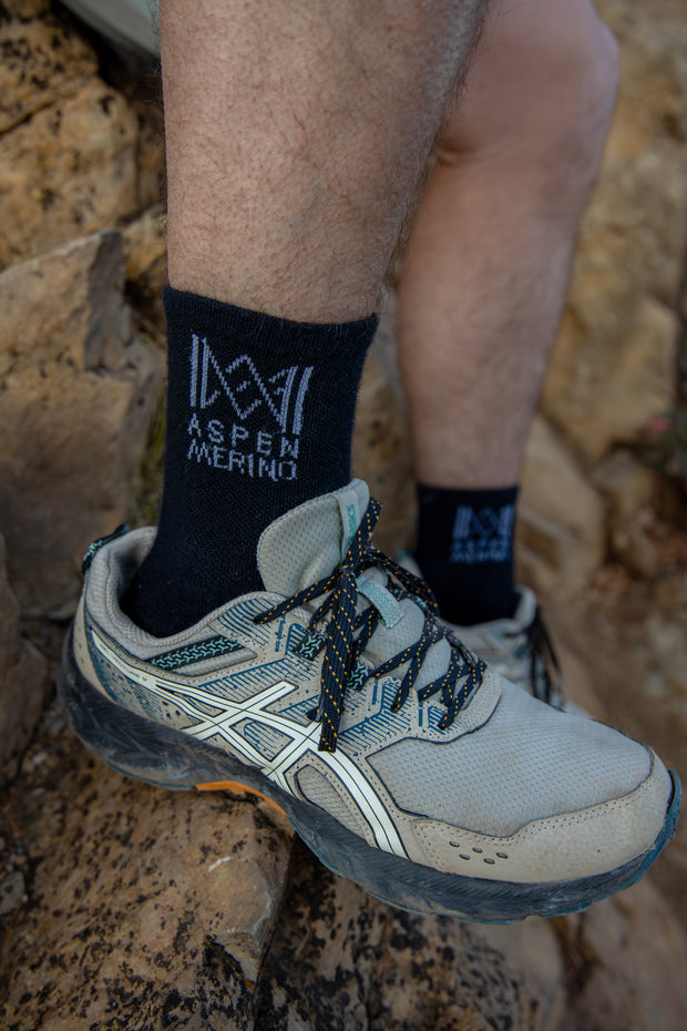 Person wearing hiking shoes and socks with 'Aspen Merino' branding on a rocky surface.