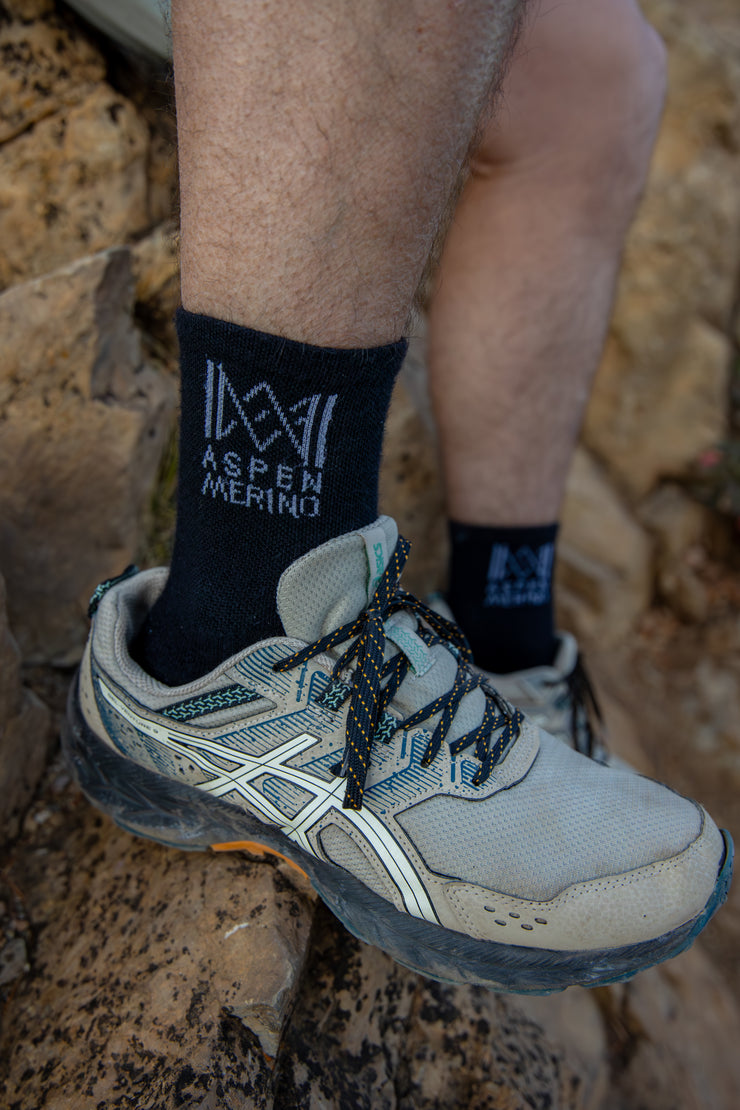 Person wearing hiking shoes and socks with 'Aspen Merino' branding on a rocky surface.