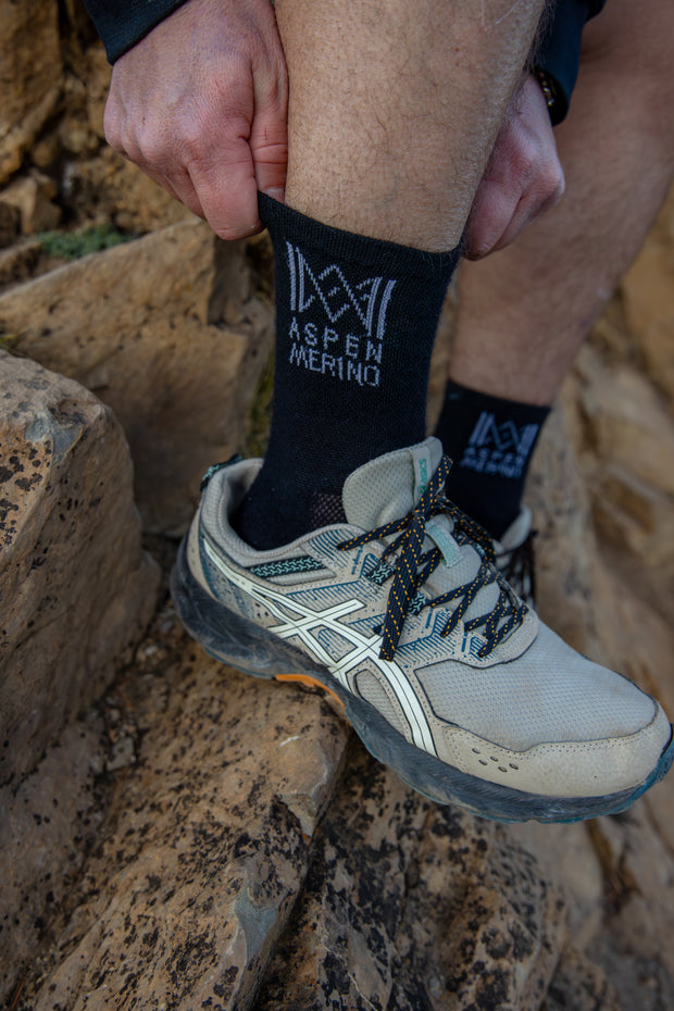 Person wearing black socks with 'Aspen Merino' branding on a stone surface