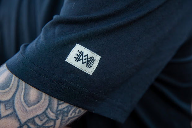 Close-up of a Men's Merino Short Sleeve with the Aspen Merino logo on the sleeve, featuring tattooed arm.