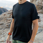 Man wearing a black Merino t-shirt standing on rocky terrain with mountains in the background